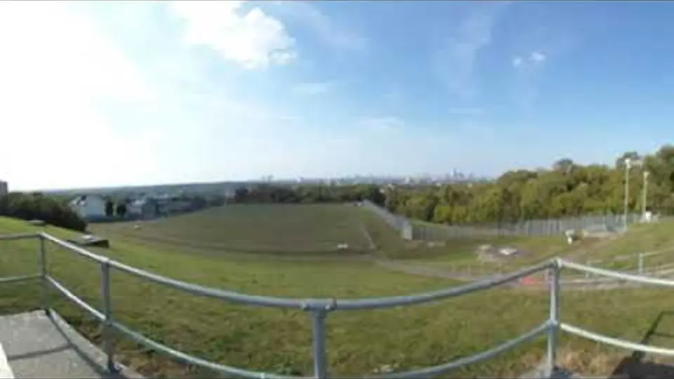 Still from a 360 degree video at the top of Nunhead Reservoir, showing the grass expanse, the handrail and the city beyond.