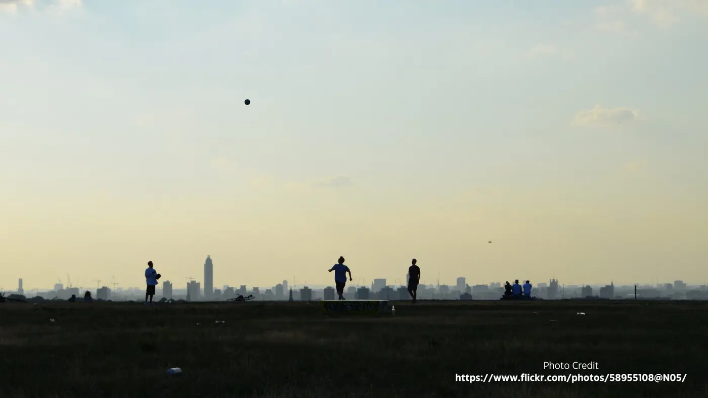 Three figures walk along the flat top of the reservoir at dusk, the city reduced to a pale silhouette behind them.