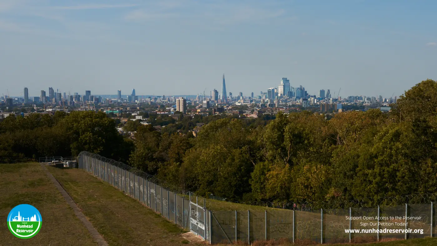 The steel security fence running the length of the reservoir, with the city visible through and above it.