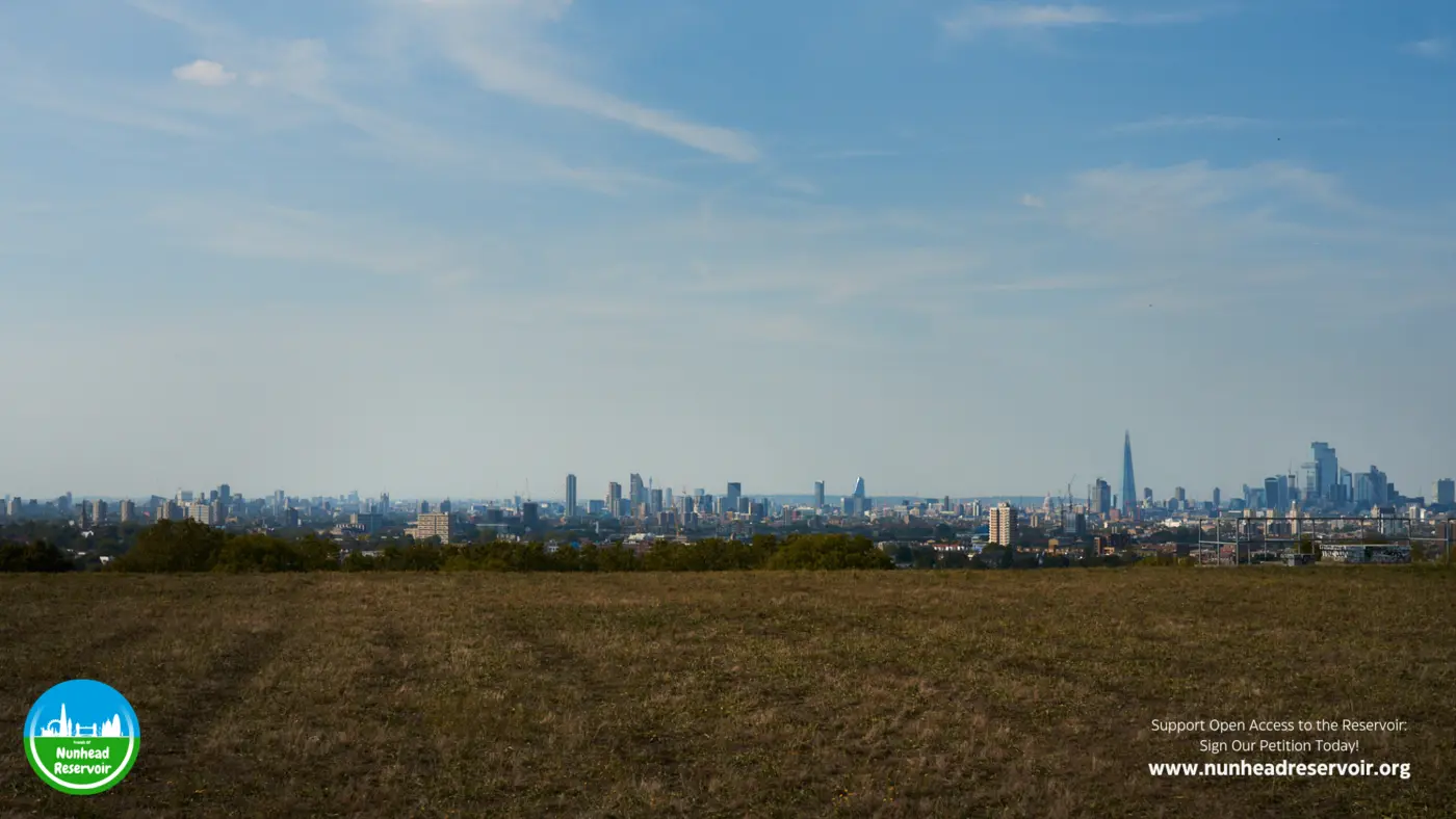 The London skyline on a hazy day seen across the reservoir, the Shard and the City towers rising out of the haze.