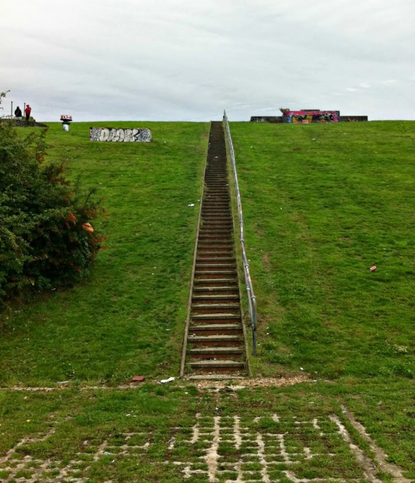 A long flight of concrete steps climbing the grass bank to the top of the reservoir, with people gathered at the summit.