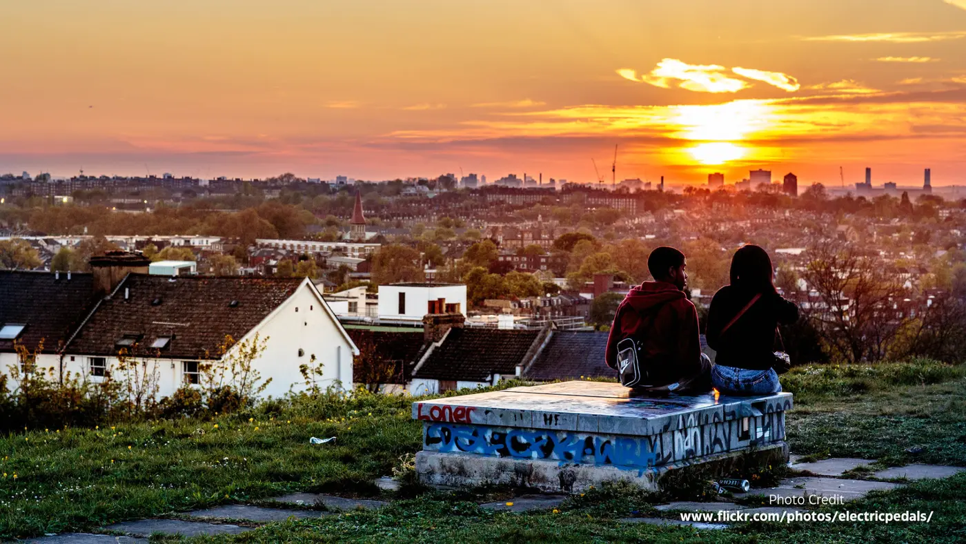 Two people sit on the concrete block watching the sun set behind the rooftops of south London.